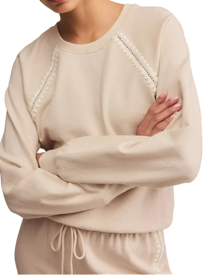 Woman wearing a beige sweater with intricate detailing on a plain background