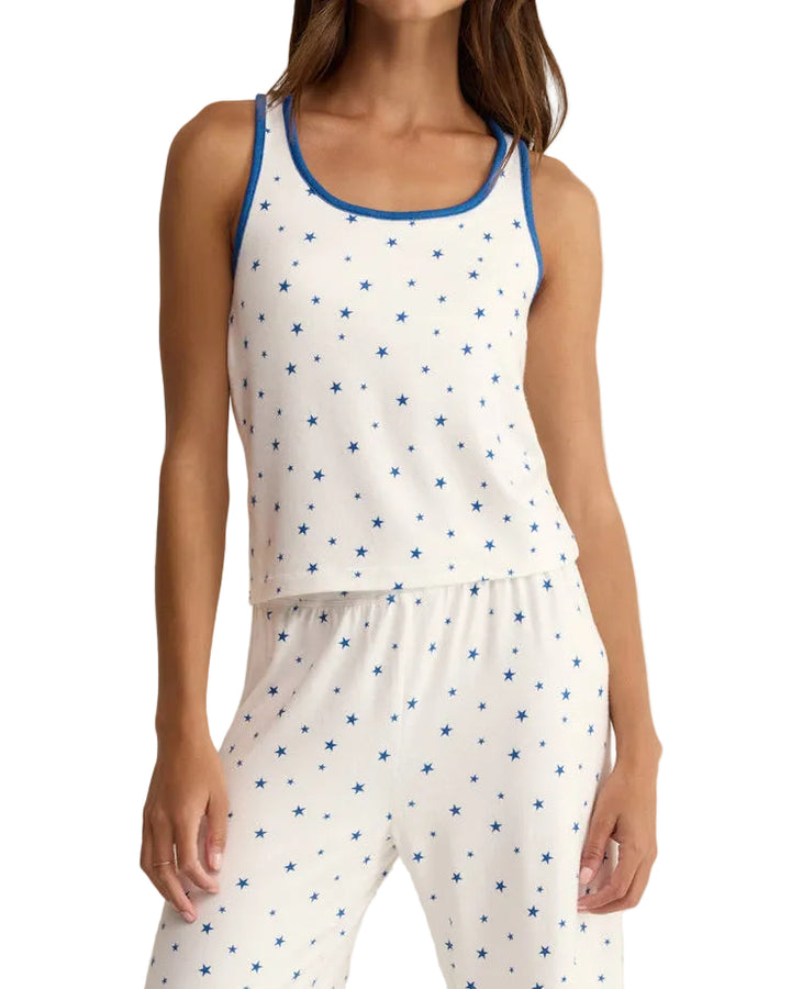 Woman wearing a white sleeveless top with blue star pattern and matching pants on a beige background