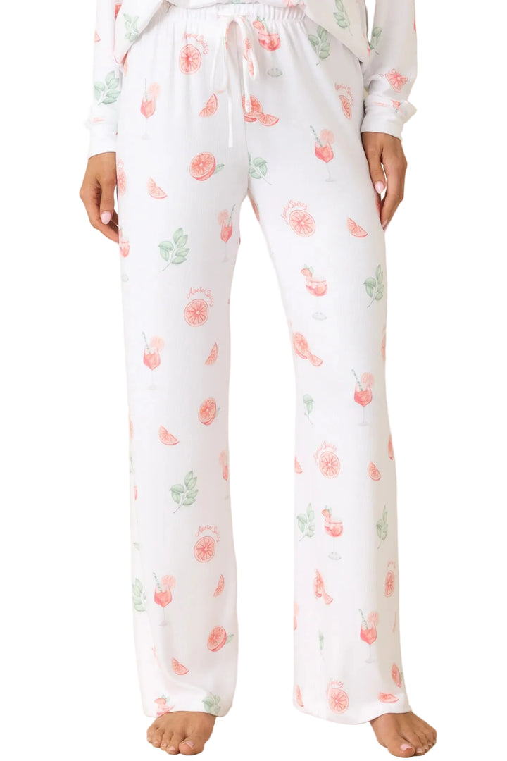 White pajama pants with a pink and green cherry print, featuring an elastic waistband with a white drawstring, shown on a model against a beige background.