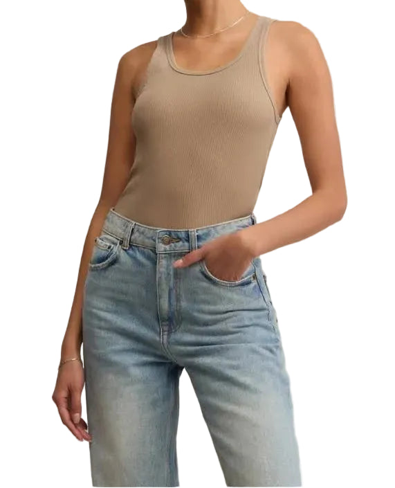 Woman wearing a beige tank top and blue jeans against a plain background