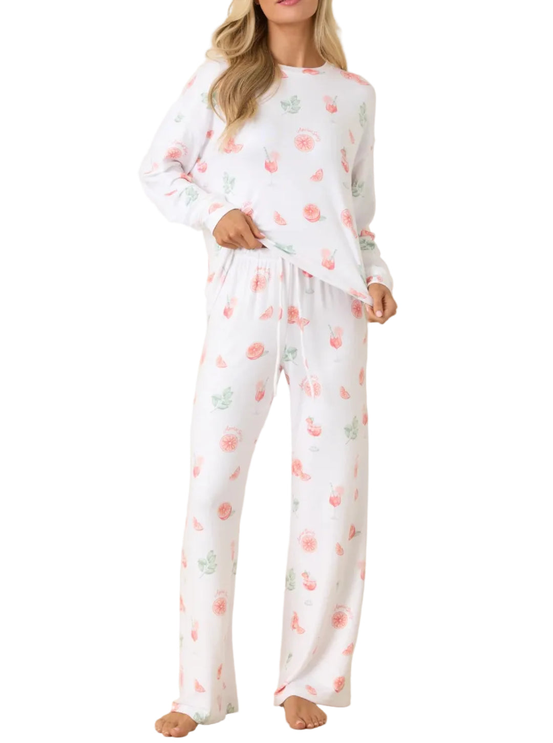 A woman modeling a white long-sleeve pajama set with a pink and green floral print, standing against a plain beige studio backdrop.