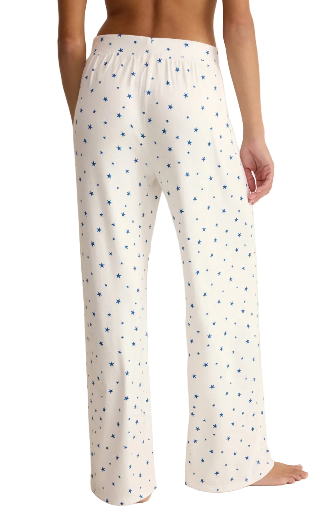 White pajama pants with blue star pattern worn by a person on a beige background