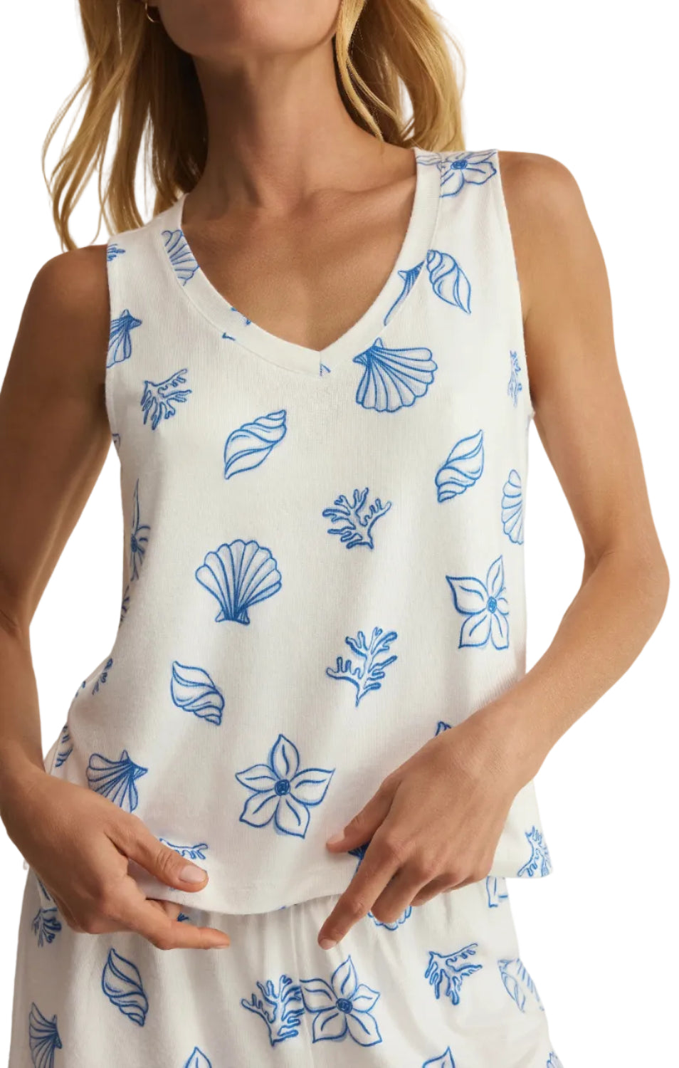 White sleeveless top with blue floral patterns worn by a person on a neutral background