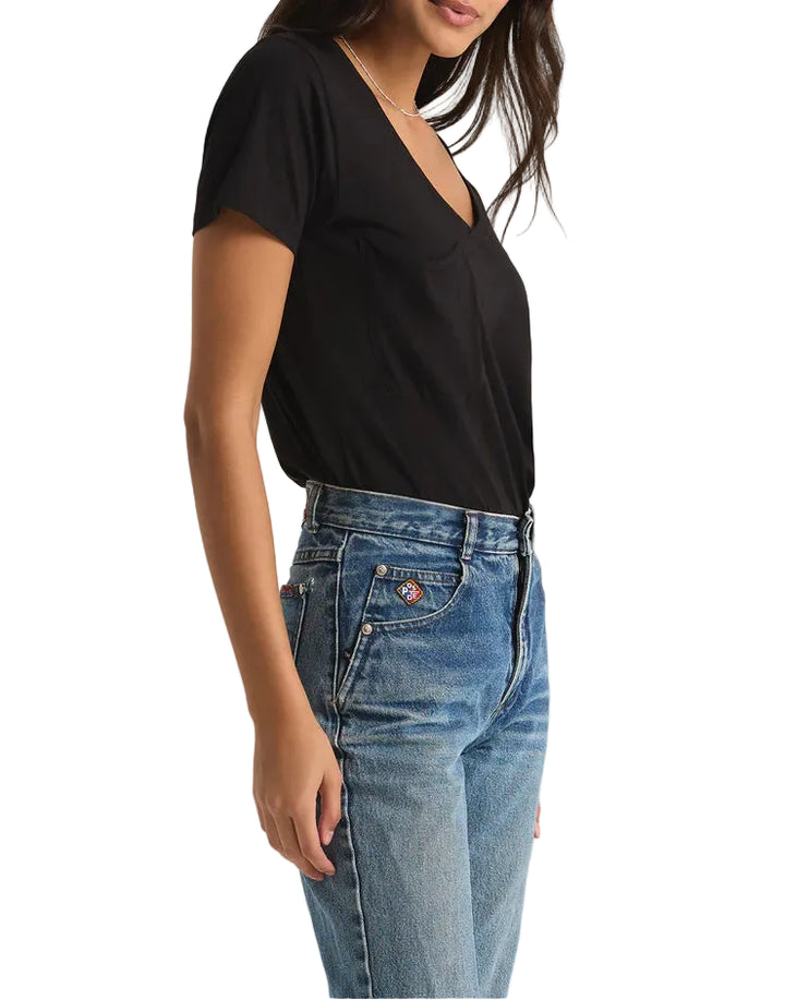 Woman wearing a black top and blue jeans against a plain background