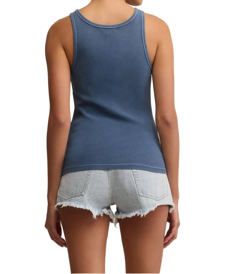 Woman wearing a blue tank top and denim shorts on a beige background