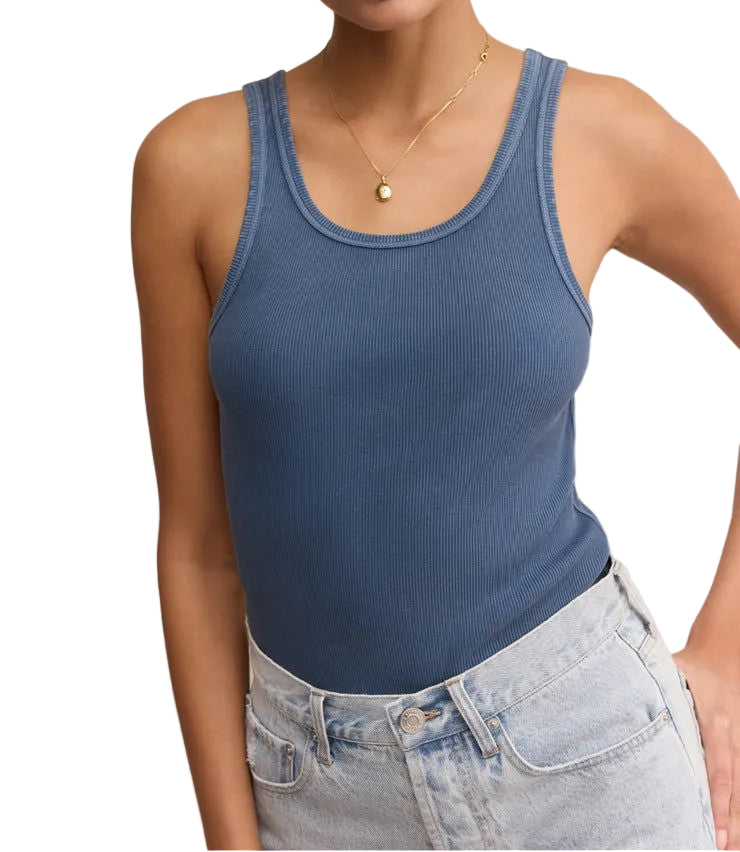 Woman wearing a blue tank top and light blue jeans against a beige background