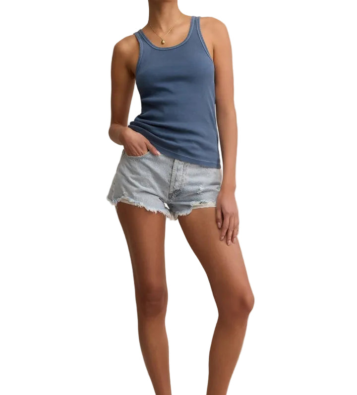 Woman wearing a blue tank top and denim shorts on a beige background