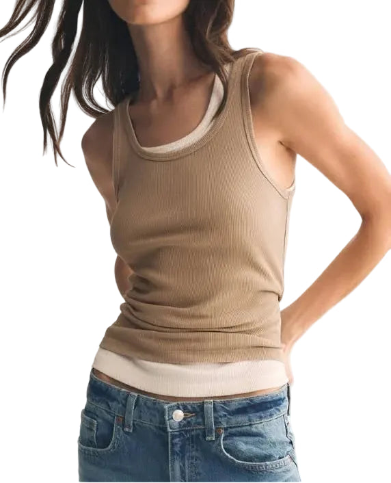 Woman wearing a beige tank top and blue jeans on a white background