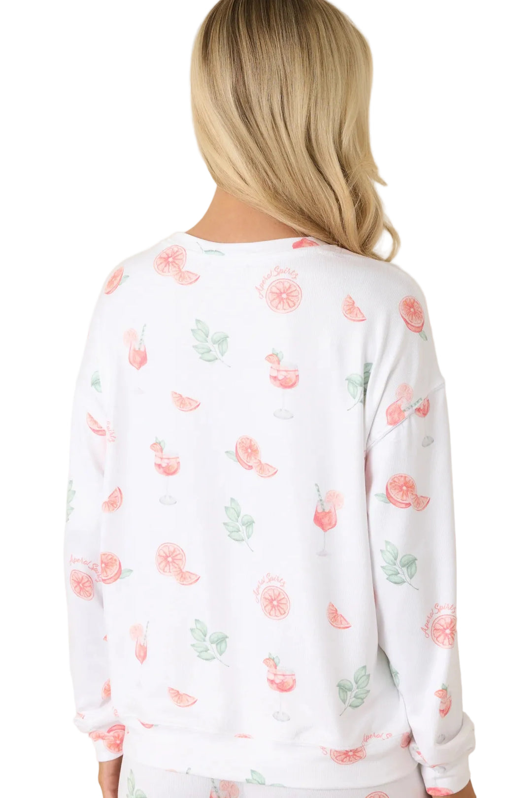 A woman shown from the back wearing a white long-sleeve crewneck sweatshirt with a scattered watercolor print of pink citrus slices, strawberries, and green leaves, set against a solid beige background.