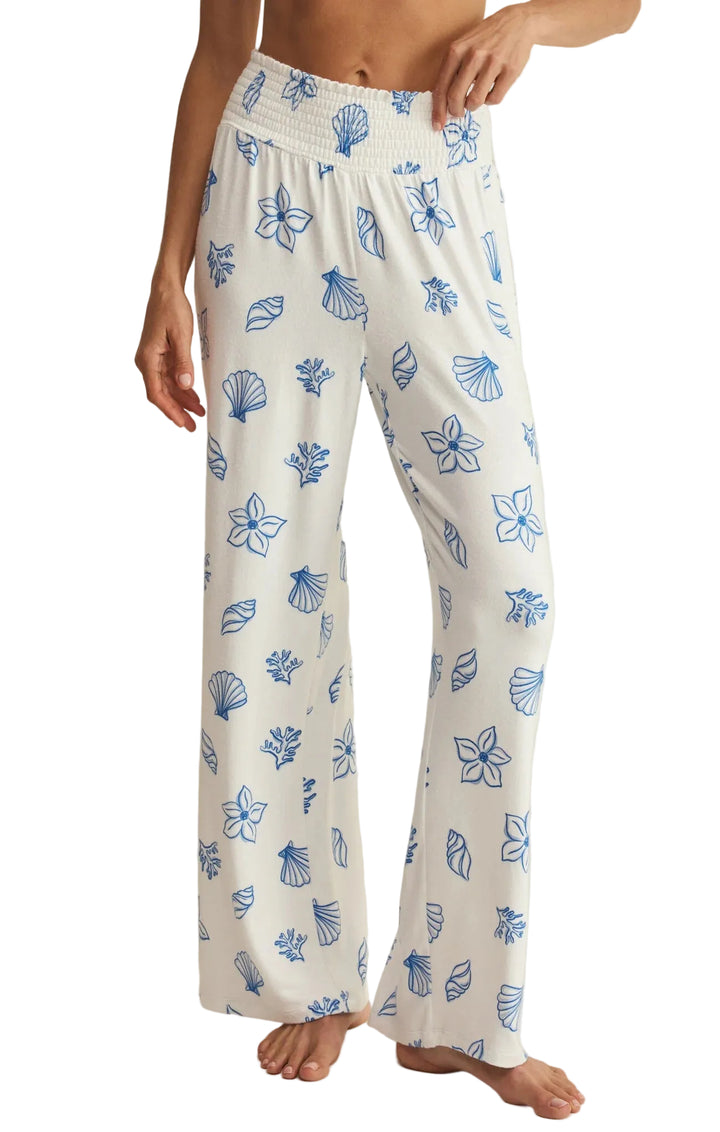 White wide-leg lounge pants with a blue floral and shell pattern, shown on a model against a light beige background.