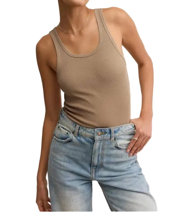 Woman wearing a beige tank top and light blue jeans against a beige background