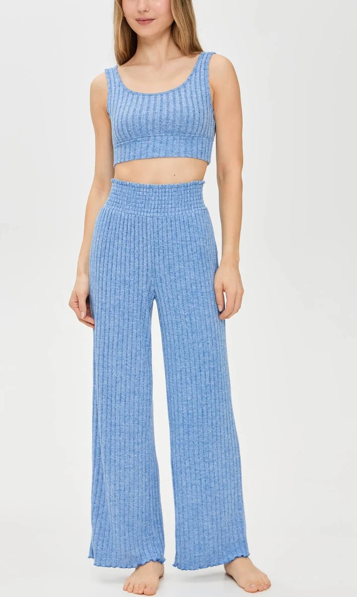 A woman modeling a light blue ribbed knit two-piece set consisting of a sleeveless crop top and high-waisted wide-leg pants, photographed against a plain white studio background.