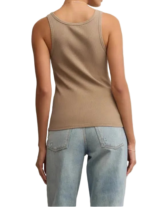 Woman wearing a beige tank top and light blue jeans against a beige background